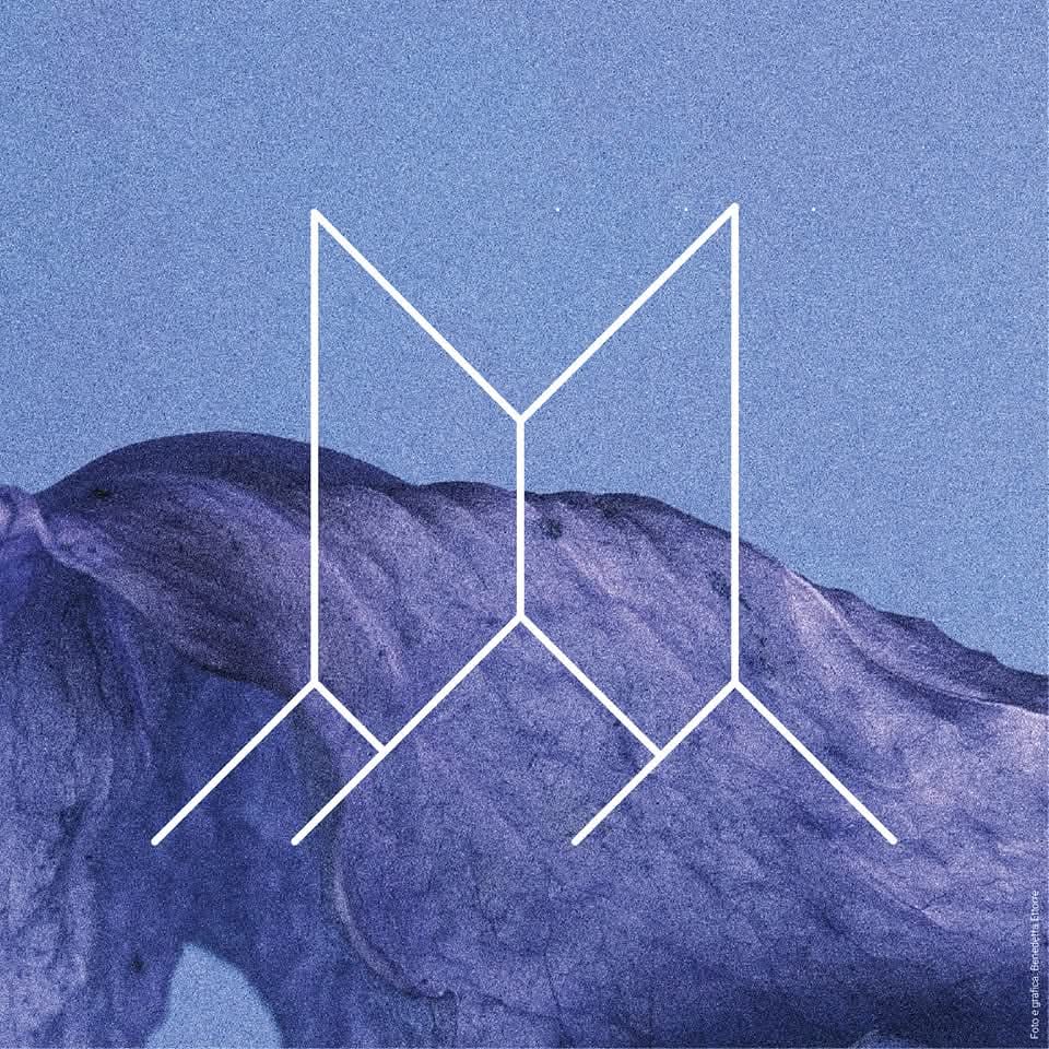 Logo Rigenera Festival. Un logo minimalista bianco di due forme geometriche stilizzate a forma di "M" su uno sfondo sfumato di blu e viola che ricorda un paesaggio montano.